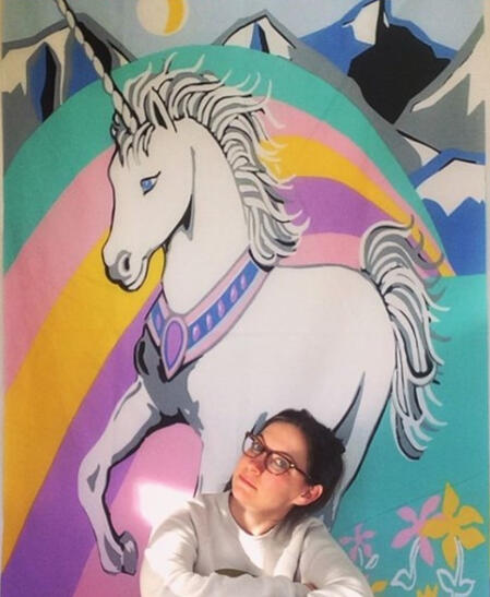 Picture of Erin Murtha , artist, in front of a unicorn backdrop she did not create